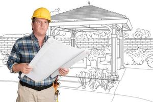 Male Contractor With House Plans Wearing Hard Hat In Front of Custom Pergola Patio Covering Drawing photo