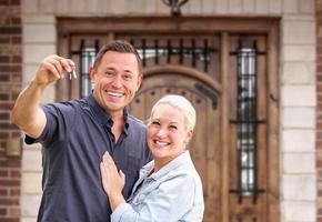 pareja joven frente a la puerta principal de la casa nueva con llaves foto