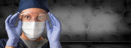 Female Doctor or Nurse Wearing Goggles, Surgical Gloves and Face Mask Against Grungy Dark Background Banner photo