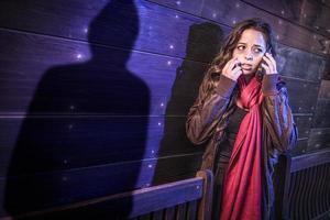 una joven adulta asustada usa un teléfono celular mientras una misteriosa figura de sombra masculina acecha cerca foto