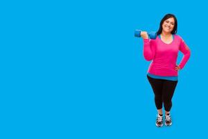 mujer hispana de mediana edad con ropa de entrenamiento sosteniendo pesas contra un fondo azul cian brillante foto