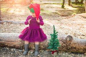 Linda niña de raza mixta divirtiéndose con sombrero de navidad y árbol al aire libre foto