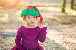 Una linda niña de raza mixta divirtiéndose usando un sombrero de navidad al aire libre foto