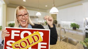 Young Woman Holding Blank Sign and Keys Inside Kitchen photo