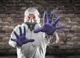 Man Wearing Hazmat Suit, Protective Gas Mask and Goggles Reaching To Stop with Hands photo