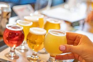 mano femenina recogiendo un vaso de cerveza artesanal de una variedad en la bandeja foto