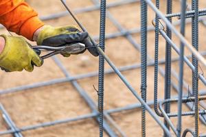 Worker Securing Steel Rebar Framing With Wire Plier Cutter Tool At Construction Site photo