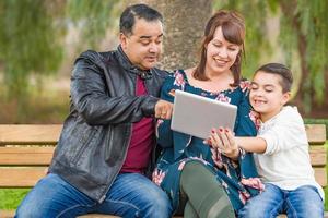 madre caucásica y padre hispano usando tableta de computadora con hijo de raza mixta al aire libre foto