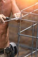 Worker Securing Steel Rebar Framing With Wire Plier Cutter Tool At Construction Site photo