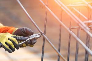 Worker Securing Steel Rebar Framing With Wire Plier Cutter Tool At Construction Site photo