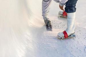 trabajador que usa zapatos con púas alisando el yeso húmedo de la piscina con una paleta foto