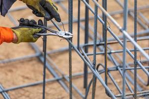 Trabajador que asegura la estructura de barras de refuerzo de acero con la herramienta de corte de alicates de alambre en el sitio de construcción foto