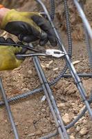 Worker Securing Steel Rebar Framing With Wire Plier Cutter Tool At Construction Site photo