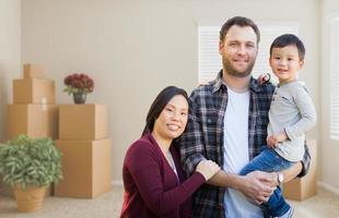 Mixed Race Chinese and Caucasian Parents and Child Inside Empty Room with Moving Boxes. photo