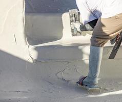 trabajador que usa zapatos con púas alisando el yeso húmedo de la piscina con una paleta foto