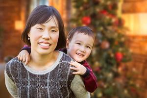 Chinese Mother and Mixed Race Child Inside House In Front of Decorated Christmas Tree. photo