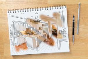 cuaderno de bocetos en el escritorio con un dibujo de la cocina y un trazo de pincel que muestra la construcción terminada junto al lápiz y la regla. foto