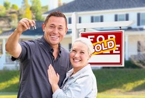 pareja de adultos jóvenes con llaves de la casa frente a la casa y se vende a la venta signo de bienes raíces foto