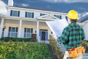 contratista masculino con casco y planes mirando la fachada de la casa personalizada. foto