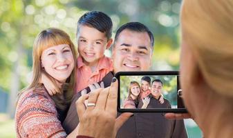 mujer tomando fotos de una familia de raza mixta con su teléfono inteligente