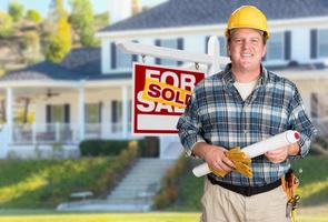 Contractor With Plans and Hard Hat In Front of Sold For Sale Real Estate Sign and House. photo