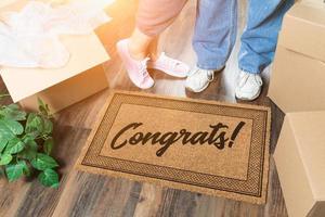 Man and Woman Unpacking Near Welcome Mat with Congrats, Moving Boxes and Plant photo