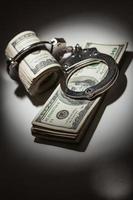 Handcuffs Locked on Roll of One Hundred Dollar Bills Under Spotlight photo