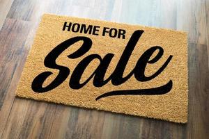 Home For Sale Welcome Mat On A Wood Floor Background photo