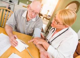 Female Nurse or Doctor Helping Senior Adult Man Take Blood Pressure In Home photo