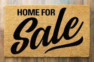 Home For Sale Welcome Mat On A Wood Floor Background photo