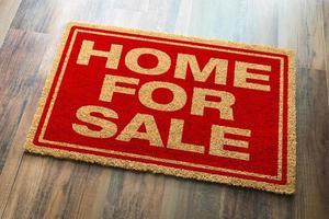 Home For Sale Welcome Mat On A Wood Floor Background photo