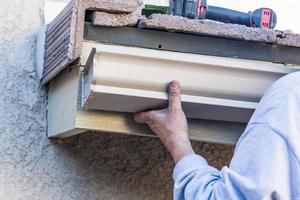 Worker Attaching Aluminum Rain Gutter to Fascia of House photo