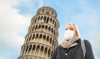 mujer joven con mascarilla camina cerca de la torre inclinada de pisa en italia foto