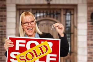 Excited Woman Holding House Keys and Sold Real Estate Sign in Front of Nice New Home photo