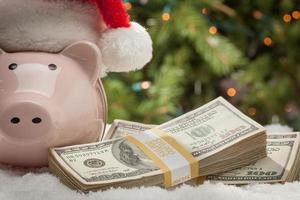 Piggy Bank Wearing Santa Hat Near Stacks of Hundred Dollar Bills on Snowflakes photo