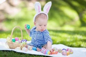 bebé de raza mixta chino y caucásico afuera usando orejas de conejo jugando con huevos de pascua foto