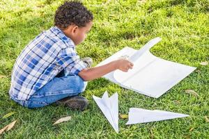 African American and Mexican Boy Learning How to Fold Paper Airplanes Outdoors on the Grass photo