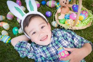 Mixed Race Chinese and Caucasian Boy Outside Wearing Rabbit Ears Playing with Easter Eggs photo