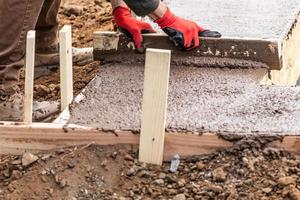 Construction Worker Leveling Wet Cement Into Wood Framing photo