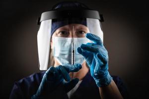 Doctor or Nurse Holding Medical Syringe with Needle AGainst Dark Background photo