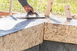 Construction Worker Using Wood Trowel On Wet Cement Forming Coping Around New Pool photo