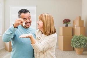 Mixed Race Couple Holding House Keys Inside Empty Room with Moving Boxes photo