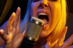 Female vocalist under gelled lighting sings with passion into condenser microphone. photo