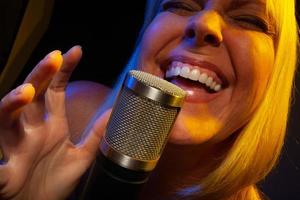 Female vocalist under gelled lighting sings with passion into condenser microphone. photo