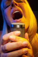 Female vocalist under gelled lighting sings with passion into condenser microphone. photo