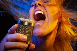 Female vocalist under gelled lighting sings with passion into condenser microphone. photo