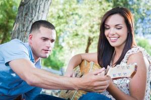 Young Adult Man Teaching Girlfriend How To Play The Guitar Outside in the Park. photo