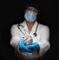 enfermera o médico con mascarilla y guantes quirúrgicos sosteniendo el planeta tierra vendado foto
