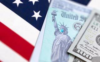 United States IRS Stimulus Check with Statue of Liberty Wearing Medical Face Mask Resting on American Flag photo