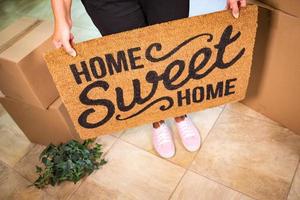 Woman in Pink Shoes Holding Home Sweet Home Welcome Mat, Boxes and Plant photo